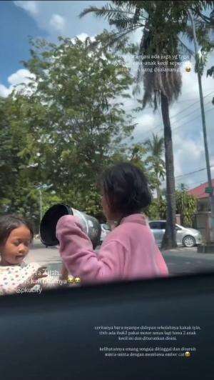 Dua anak kecil, menggunakan kostum badut dan membawa ember kosong, diturunkan ibu-ibu yang mengendarai NMAX.

Setelah menurunkan anak-anak, 